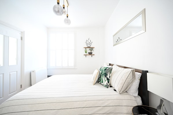 A neatly arranged bedroom with a large bed, a bedside table, a mirror, and a shelf with plants. - The Teapot Cottage 🫖 in Town Centre. (Stratford-upon-Avon)