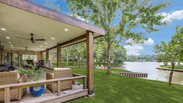 Un espacio exterior techado con mobiliario de mimbre, una parrilla y vistas a un lago.