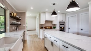Una cocina moderna con armarios blancos, encimera de mármol y dos lámparas colgantes.
