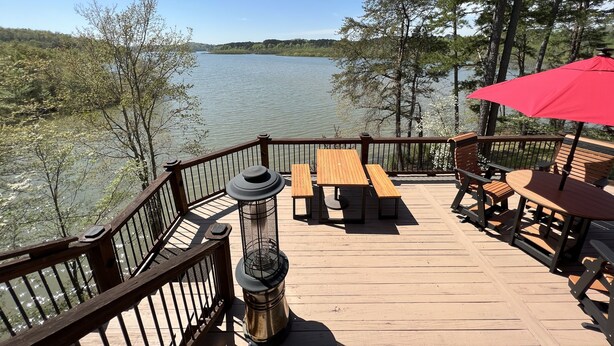 A wooden deck with outdoor seating and a red umbrella, overlooking a calm lake surrounded by trees. - Perfect relaxing lake retreat for hosting a gathering. Quiet with no neighbors. (Westminster)