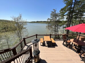 Eine Holzterrasse mit Sitzgelegenheit und einem roten Sonnenschirm, mit Blick auf einen stillen See, der von Bäumen umgeben ist.
