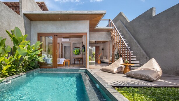 A modern outdoor pool area with a wooden deck, lounge chairs, and a staircase leading to an upper level. - Agrapana Beach Villa (Sukawati)
