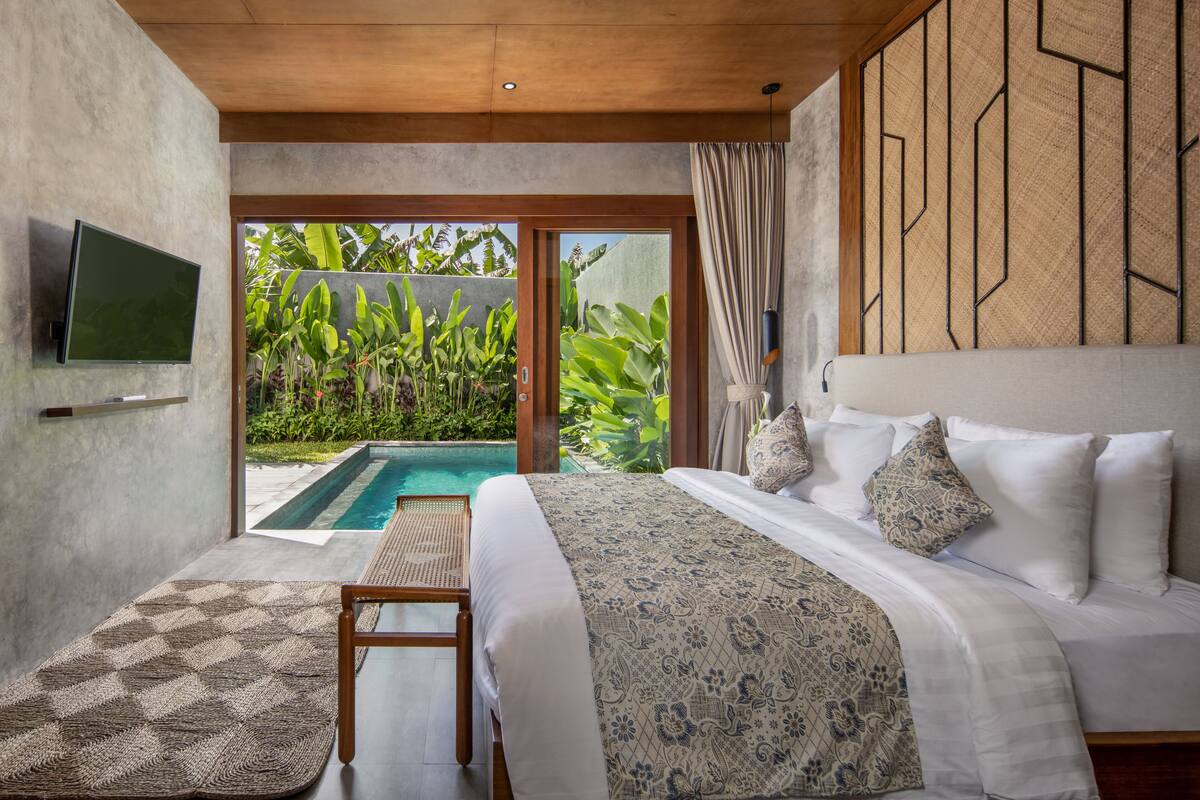 A bedroom with a large bed, a television, and a view of a swimming pool.