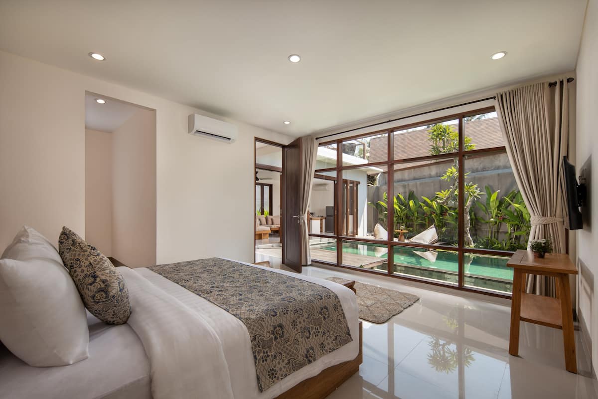 A bedroom with a large bed, a view of a swimming pool, and a TV mounted on the wall.