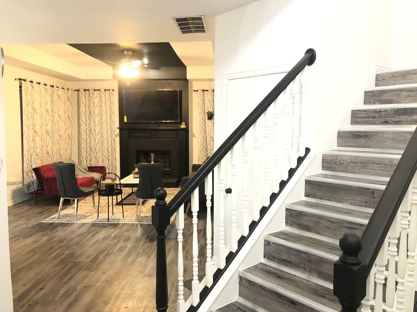 A modern living room with a fireplace, a staircase with white balusters, and a red sofa.