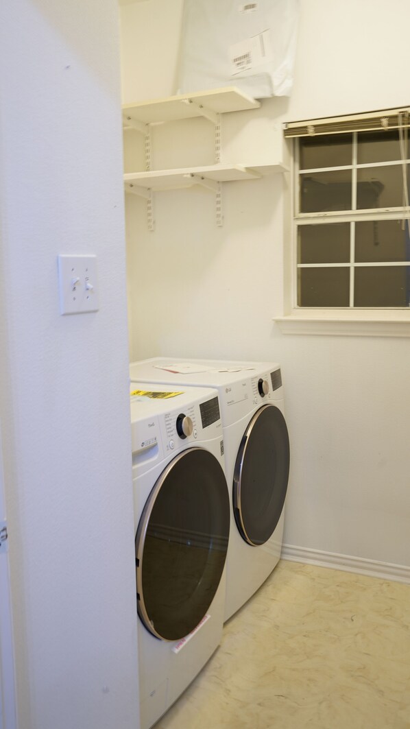 A laundry room with two front-loading washing machines and a window with blinds. - Remodeled luxury with Proximity (Lewisville)