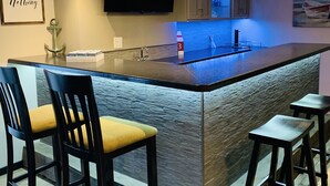 A modern kitchen with a central island, bar stools, a flat-screen TV, and a stone-textured backsplash. - Home w/ hot tub, game room, sauna on Lake Wausau near Granite Peak (Schofield)