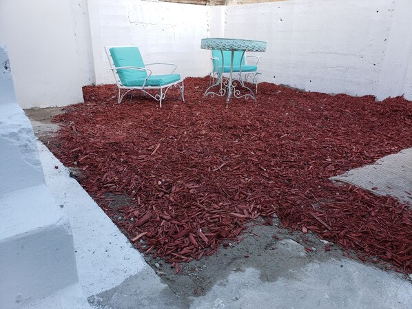 Un pequeño espacio exterior con dos sillas metálicas turquesa y una mesa a juego, rodeado de acolchado rojo.