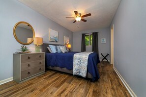 A bedroom with a bed, dresser, ceiling fan, and artwork on the walls.