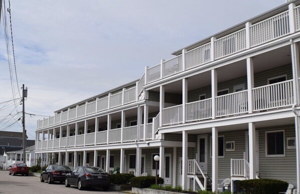 A multi-story hotel with balconies, a covered front porch, and a parking area with cars.