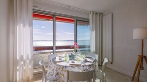 Zona pranzo con tavolo imbandito per due, vista sul mare e lampada su un supporto in legno.