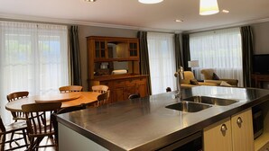 Een moderne keuken met een centraal eiland, een houten eettafel en stoelen. Er is een inbouwkast en een televisie in de hoek.