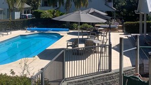 Een zwembad met een omliggend terras, tuinmeubilair en palmbomen.