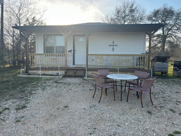Une petite maison avec un porche, une table ronde entourée de chaises et une terrasse en bois.