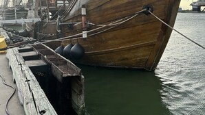 Een groot houten schip afgemeerd aan een steiger, met zichtbare touwen en redijboeiën.