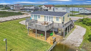 Een huis met twee verdiepingen, voorzien van een balkon, een terras en een kleine steiger die in het water uitkomt.