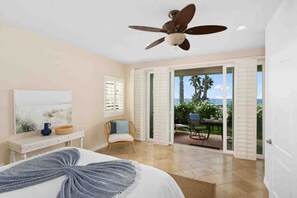 A bedroom with a bed, a ceiling fan, a window with shutters, a chair, and a view of the outdoors. - Spacious Beach House • Walk to Beach, Pier & Downtown (Oceanside)