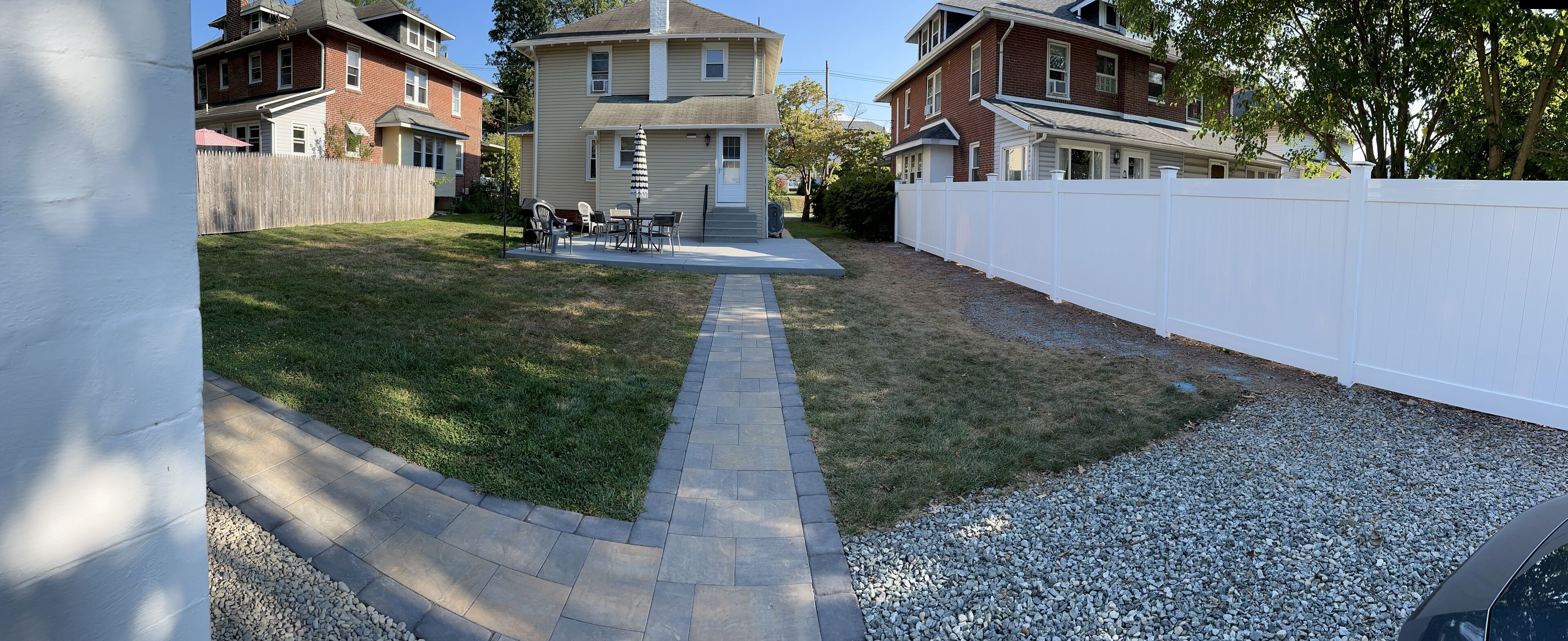 Ein Garten mit gepflastertem Weg, weißem Zaun und Rasenfläche.