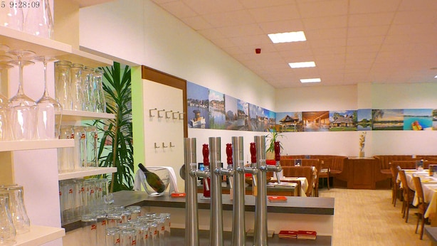 A restaurant interior with a bar area, wine glasses on shelves, and a seating area with tables and chairs. - Hotel B3 (Mauthausen)