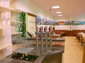 Interior de restaurante con barra, copas de vino en estanterías y zona de comedor con mesas y sillas.