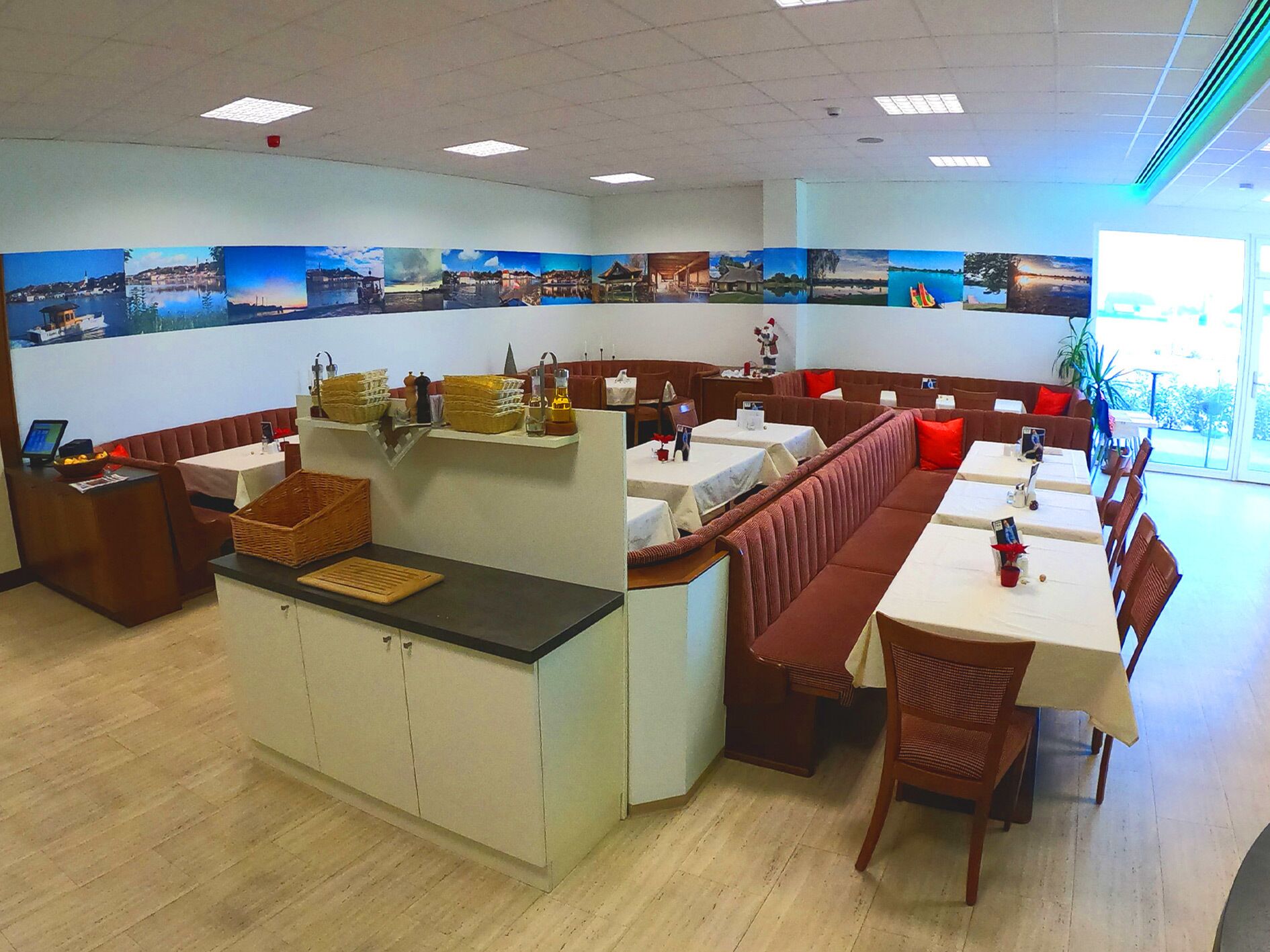 Un restaurant avec des banquettes et des tables, un comptoir avec des paniers, et un mur décoré de tableaux représentant des paysages.