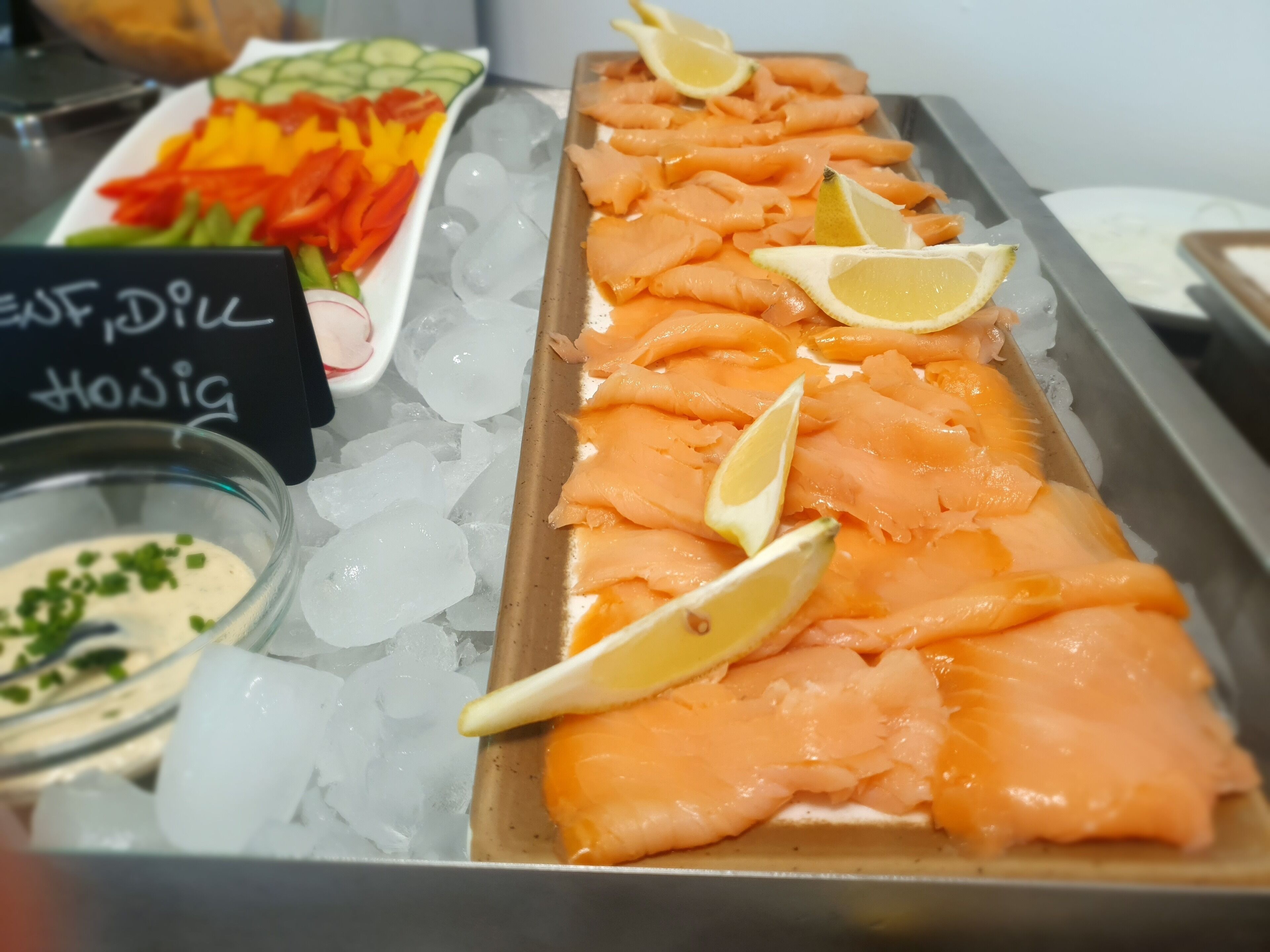 Una presentación de salmón sobre hielo con rodajas de limón, un tazón de salsa y un letrero que dice "Fresh Dill Hovis".