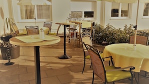 An outdoor patio area with tables and chairs, umbrellas, and potted plants. - Hotel B3 (Mauthausen)