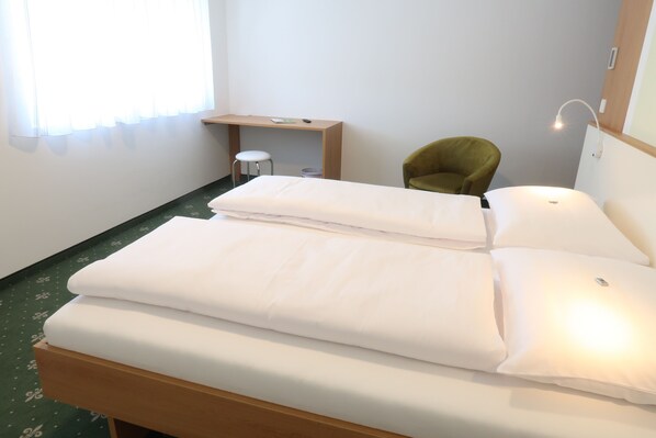 A hotel room with a bed, a desk, a chair, and a small stool.