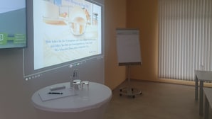 A hotel room with a projector screen displaying a welcome message, a whiteboard with a handwritten note, and a small table with a notebook and pen. - Hotel B3 (Mauthausen)