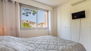 Ein Schlafzimmer mit einem Bett, einem Fenster, einem an der Wand befestigten Fernseher und einer Klimaanlage.