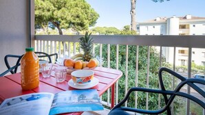 Ein Balkon mit einem für ein Frühstück gedeckten Tisch, mit Früchten und einem Getränk, mit Blick auf ein Wohngebiet mit Bäumen und Häusern.