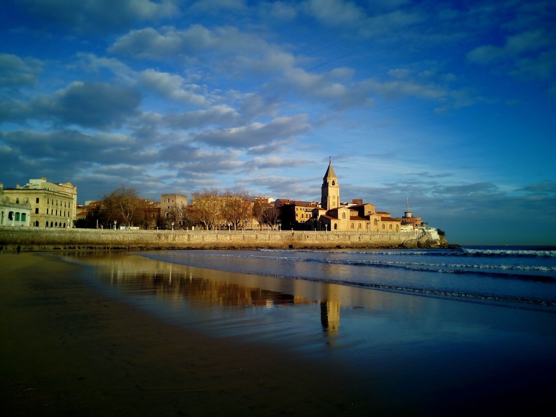 Un paisaje urbano costero con una torre destacada y edificios históricos a lo largo del paseo marítimo.