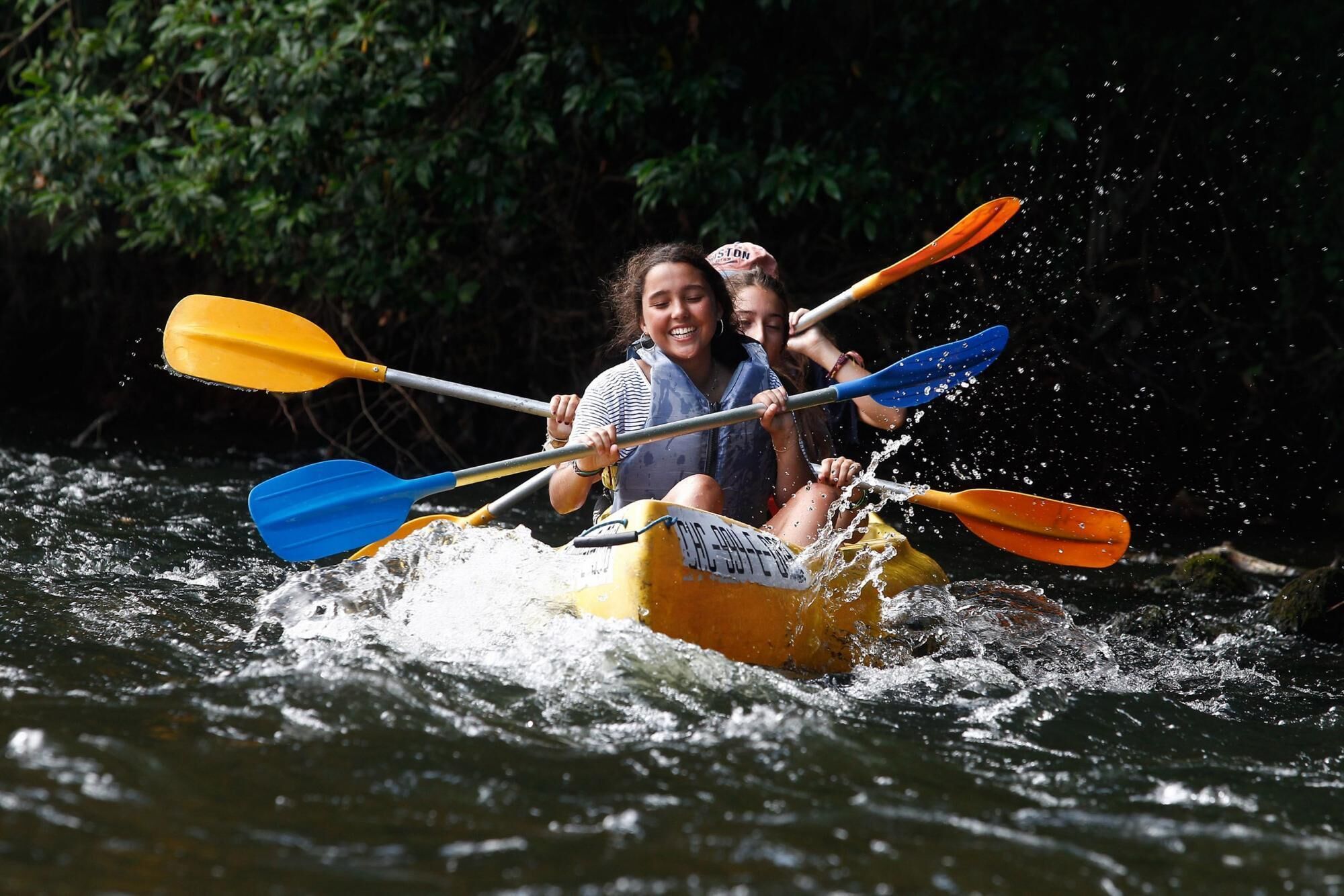 Two people kayaking on a river surrounded by dense foliage.
