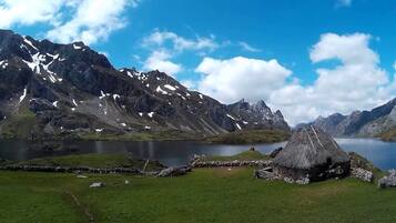 A mountain landscape with a lake and a thatched-roof hut.