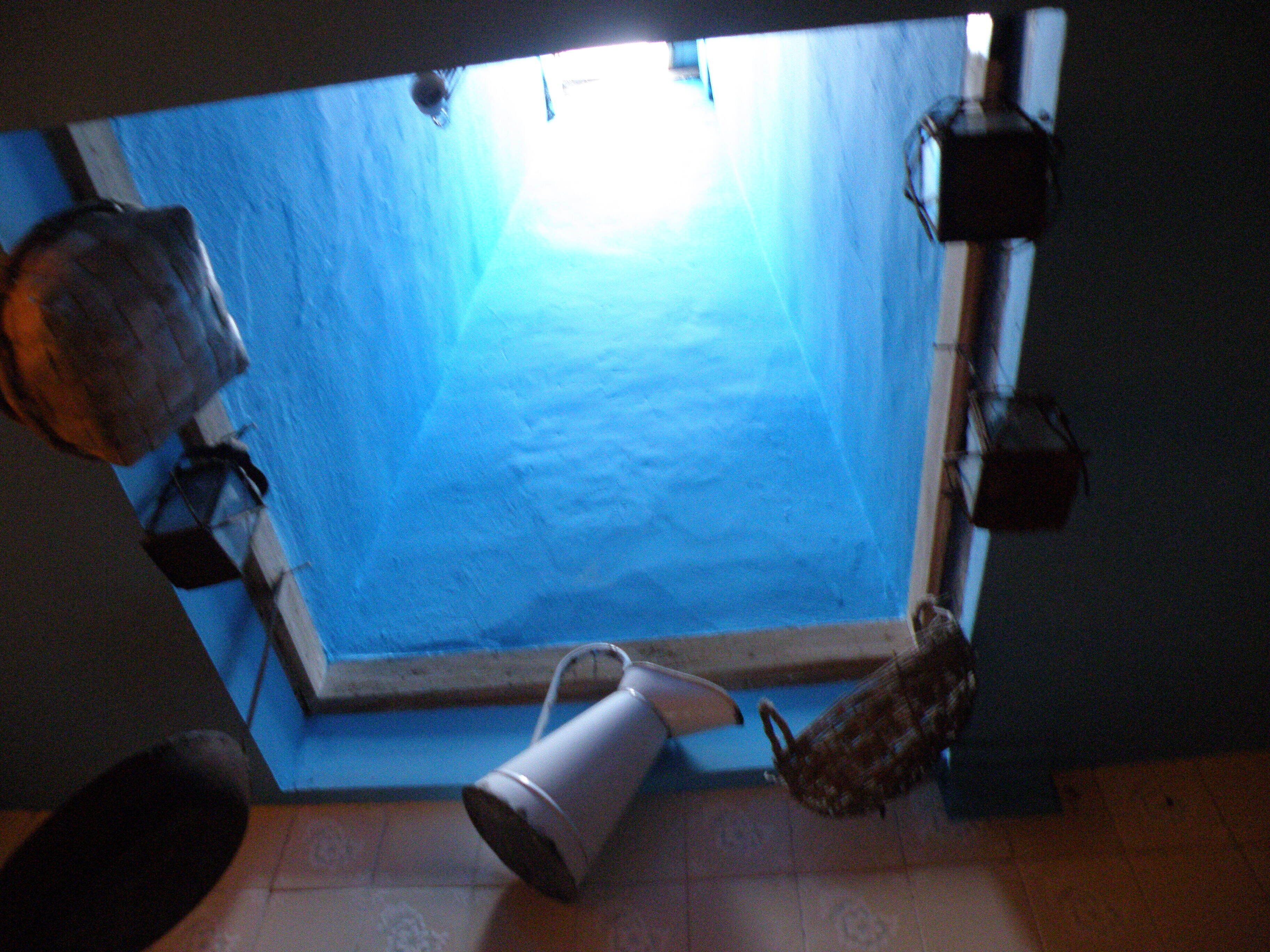 Una habitación con tragaluz, una ventana y un cubo de metal en el suelo.