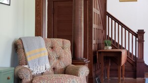 Een gestreept fauteuil met een plaid, een houten trap en een ingelijste botanische illustratie aan de muur.