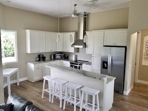A modern kitchen with white cabinets, a stainless steel refrigerator, a built-in island with bar stools, and a ceiling fan. - Beautiful Vacation House Close to the Beach (Venice)