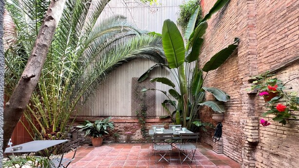 Een terras met een bakstenen muur, potplanten en een tafel met stoelen.