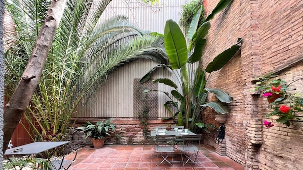 Une terrasse avec un mur en briques, des plantes en pot et une table avec des chaises.