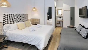Une chambre d’hôtel moderne avec un grand lit, un petit canapé, une tête de lit en bois, un miroir, une télévision et une salle de bain équipée d’un lavabo et d’un miroir.