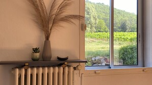 A room with a radiator, a window with a view of greenery, and a shelf with a plant and decorative items. - Quiet wine-growing estate in the heart of nature, ideal for family vacations (Brignoles)