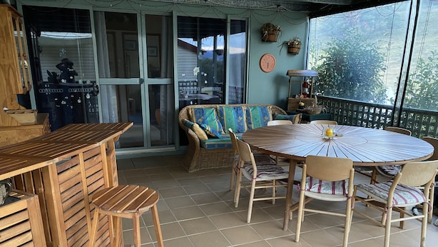 Un patio couvert avec une table ronde en bois et des chaises, un canapé en osier et un comptoir de bar en bois.