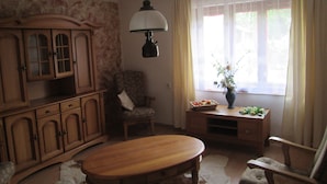 Uma sala de estar com um armário de madeira, uma cadeira, uma mesa e uma janela com cortinas.