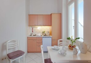 Een kleine keuken met witte kastjes, een wit aanrechtblad en een eethoek met een tafel gedekt voor twee personen.