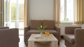 Una sala de estar con sofá, dos sillones, una mesa de centro y un ventanal con cortinas.