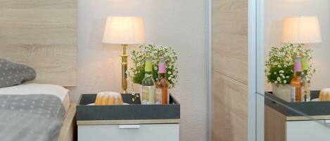 A neatly arranged bedroom with a bed, bedside tables, a mirror, and a nightstand with a lamp and flowers.