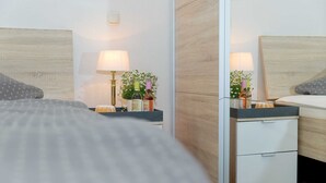 Una habitación de hotel moderna con cabecera de madera, una mesita de noche con lámpara, una planta pequeña y un mueble auxiliar con espejo.