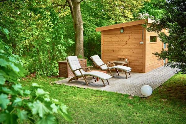 A wooden cabin with a deck, two lounge chairs, and a small table.