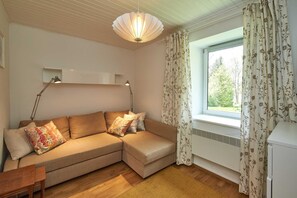 Una sala de estar con sofá, dos lámparas, una ventana con cortinas y un radiador.