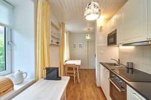 A compact kitchen with a wooden countertop, a microwave, a stove, and a window with a curtain.